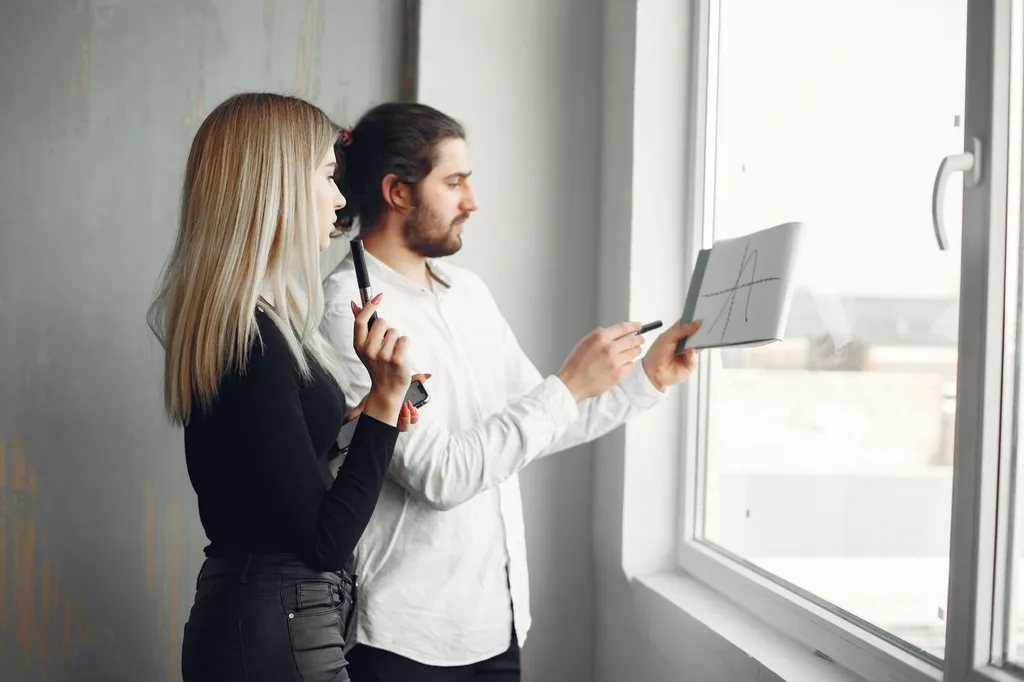 Two colleagues collaborating on a project by a window, promoting teamwork and innovation.